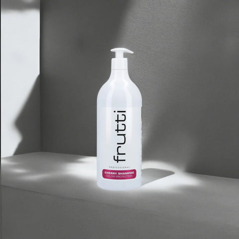 butelka z białym szamponem Frutti Professional Cherry Shampoo do włosów farbowanych, z czarnymi literami, ustawiona na jasnej powierzchni z dramatycznym cieniem i światłem tworzącym kontrastowe linie na tle szarej ściany