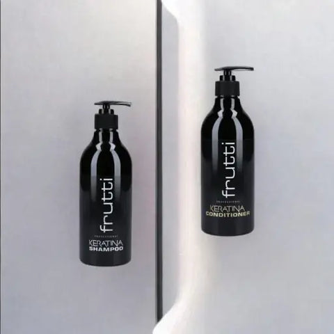 Opakowania szamponu i odżywki Frutti Professional Keratin, o eleganckim czarnym designie z białymi etykietami i napisami, stoją obok siebie na błyszczącej białej powierzchni podzielonej na dwa panele przez pionową linie odbijającego światła, co dodaje kompozycji współczesnego i profesjonalnego wyglądu