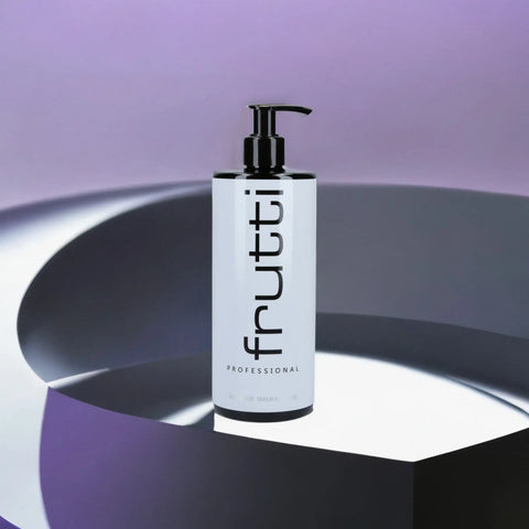Butelka z fioletowym szamponem Frutti Professional Silver do włosów blond, umieszczona na geometrycznym podium w odcieniach purpury i szarości, tworząc elegancką, nowoczesną prezentację na tle ombre od fioletu do białego.