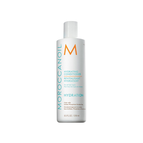 Zdjęcie produktu ukazuje cylindryczną, białą butelkę odżywki Moroccanoil Hydrating Conditioner o pojemności 250 ml. Na przodzie widnieje duże, pionowe logo "MOROCCANOIL" w kolorze turkusowym oraz duża pomarańczowa litera "M". Poniżej znajdują się nazwy produktu w języku angielskim i francuskim oraz informacja, że produkt jest bezpieczny dla koloru i wolny od siarczanów, fosforanów i parabenów. Butelka ma białą nakrętkę i znajduje się na tle z szachownicą przezroczystości.