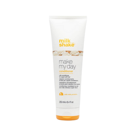 Zdjęcie produktu przedstawiające odżywkę do włosów milk_shake z linii "make my day" w tubie o pojemności 250 ml. Opakowanie jest białe z pomarańczowym logo marki i grafiką bitej śmietany w centralnej części. Poniżej znajduje się nazwa serii oraz informacja o zawartości protein mleka ("with milk proteins"). Tuba posiada pomarańczowe zamknięcie typu flip-top i jest przedstawiona na tle szachownicy symbolizującej przezroczystość.